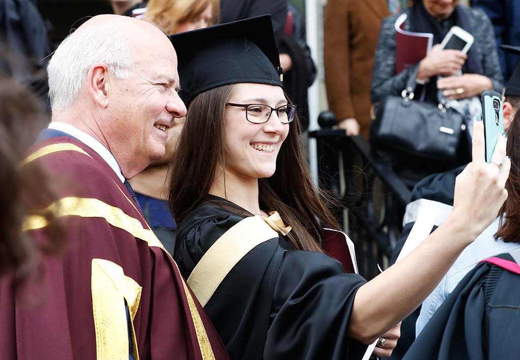 Chancellor Peter Mansbridge stopping for a selfie with a graduating student.